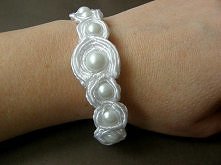 Wykonana ręcznie z dużą dokładnością i precyzją z perełek i atłasowej tasiemki,w kolorze bieli. Bransoletka zapinana na typowy karabińczyk, przedłużona łańcuszkiem w kolorze sre...