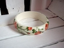 Drewniana, zaokrąglowa bransoletka ozdobiona decoupage w delikatne róże. Kilkukrotnie lakierowana. Wysokość 2cm, średnica wewnętrzna 6,7cm. Rozmiar uniwersalny.