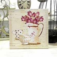 Kwadratowy obraz z bukietem tulipanów w dzbanie, kubkiem i dwoma miseczkami , na jasnym tle dzięki czemu widoczny w nim jest styl prowansalski.