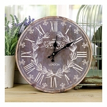 Ciemny okrągły zegar retro ozdobiony wieńcem laurowym w jasnym kolorze, z rzymskimi cyframi. Jego urok tkwi w wykończeniu go na lekko starodawny styl.