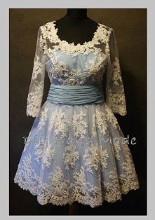 Sukienka o rozkloszowanym kroju. Uszyta z satyny grubej i koronki koder/gipiury. Odcinana w talii szerokim marszczonym pasem. Wersja z dlugim rekawem.