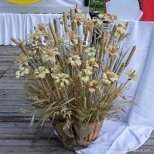 Kwiaty ze słomy prasowane i plecione, umieszczone w wiklinowym koszu.