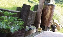 Brązowy zbiornik na wodę opadową, przymocowany do rynny, która zbiera deszczówkę z dachu. Polecamy szczególnie ze względu na kolor i fakturę wykończenia powłoki zewnętrznej, któ...